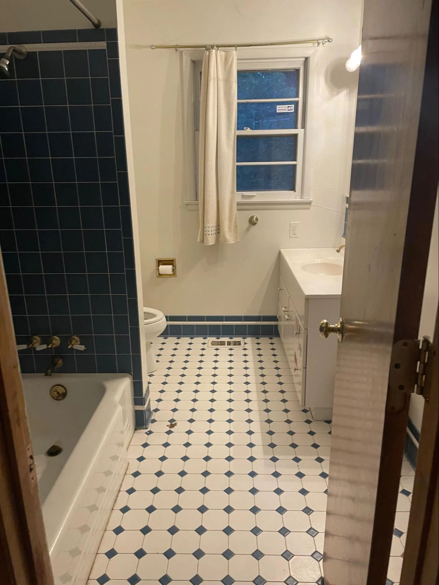 Dated bathroom with hand-painted navy tiles, worn fixtures, aged vanity sink, and outdated design requiring bathroom remodeling