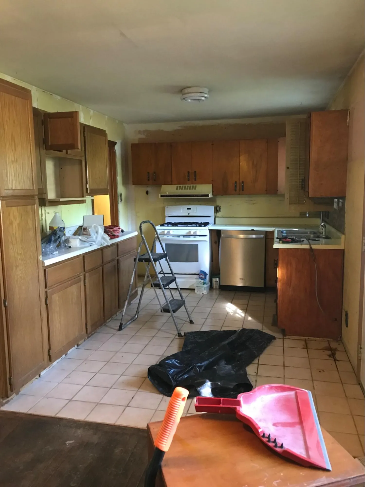 Kitchen before renovation showing worn cabinets, dated appliances, and worn flooring